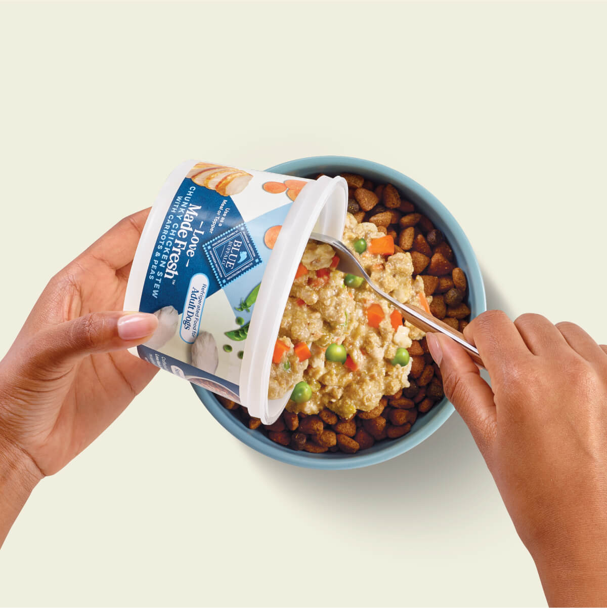 A Pet Parent scoops BLUE Love Made Fresh on top of a bowl of dry dog food.